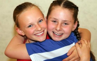 A girl in a blue t shirt hugs a girl in a red t shirt they both look very happy